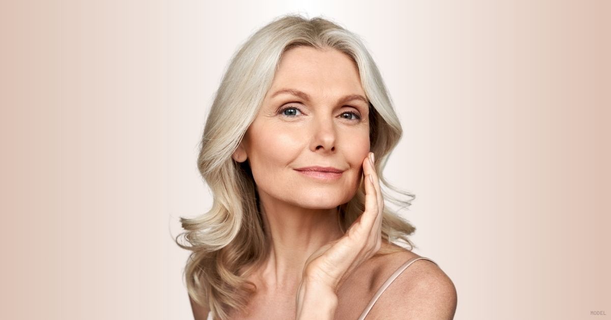 Mature woman smiling and touching her face. (Model)